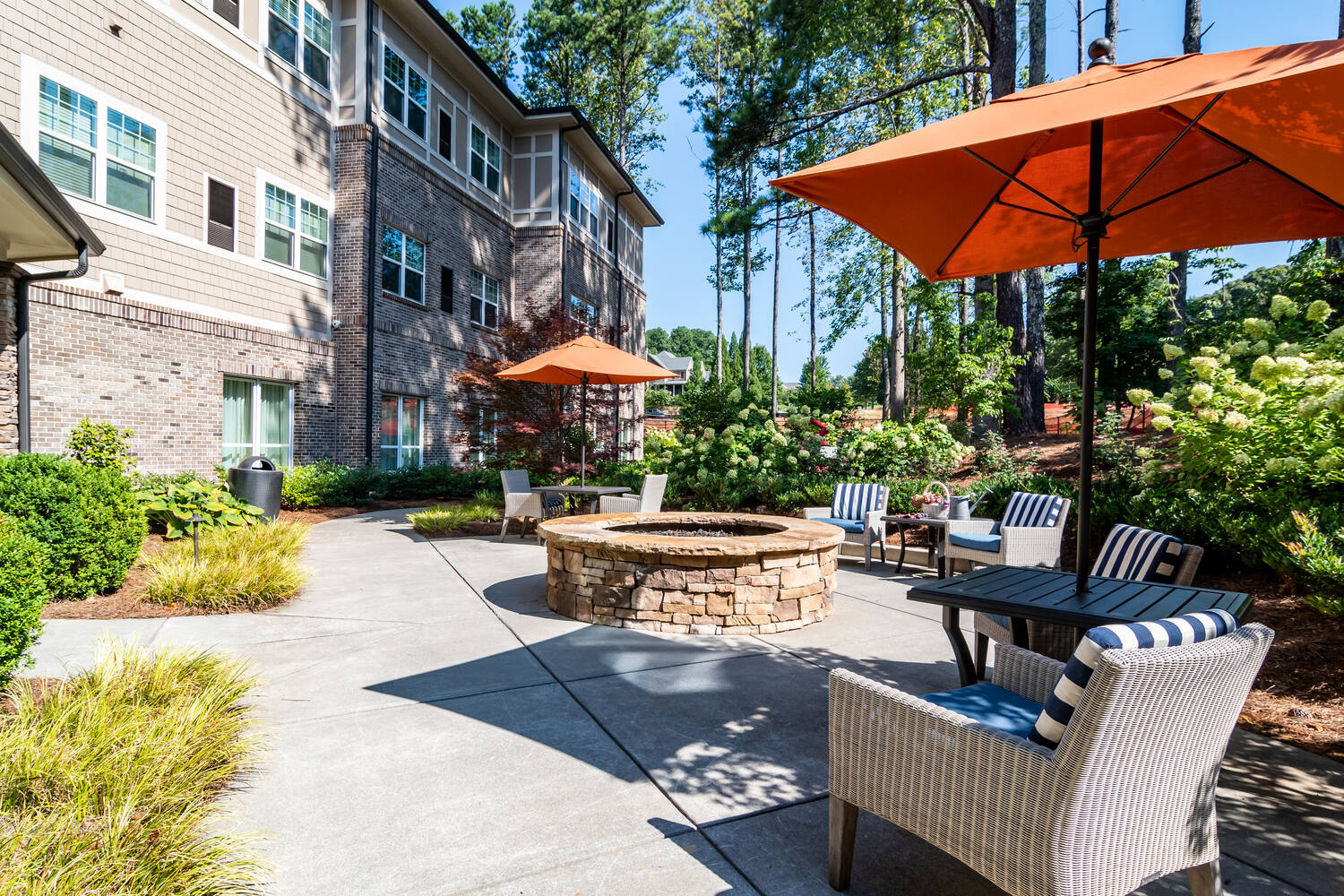 A cozy outdoor patio with a stone fire pit, umbrella seating, and lush greenery at Arbor Terrace Burnt Hickory, a senior living community in Marietta, GA.