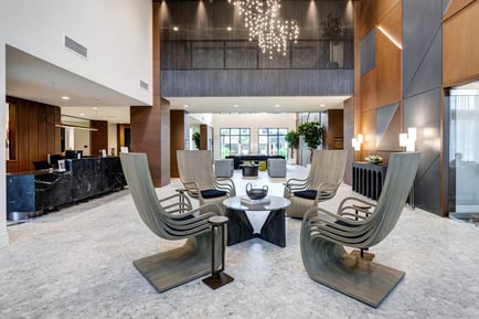 A grand lobby featuring a sparkling chandelier, sculptural lounge chairs around a round table, and a marble front desk, reflecting the resort-style amenities of senior living in Delray Beach, FL.